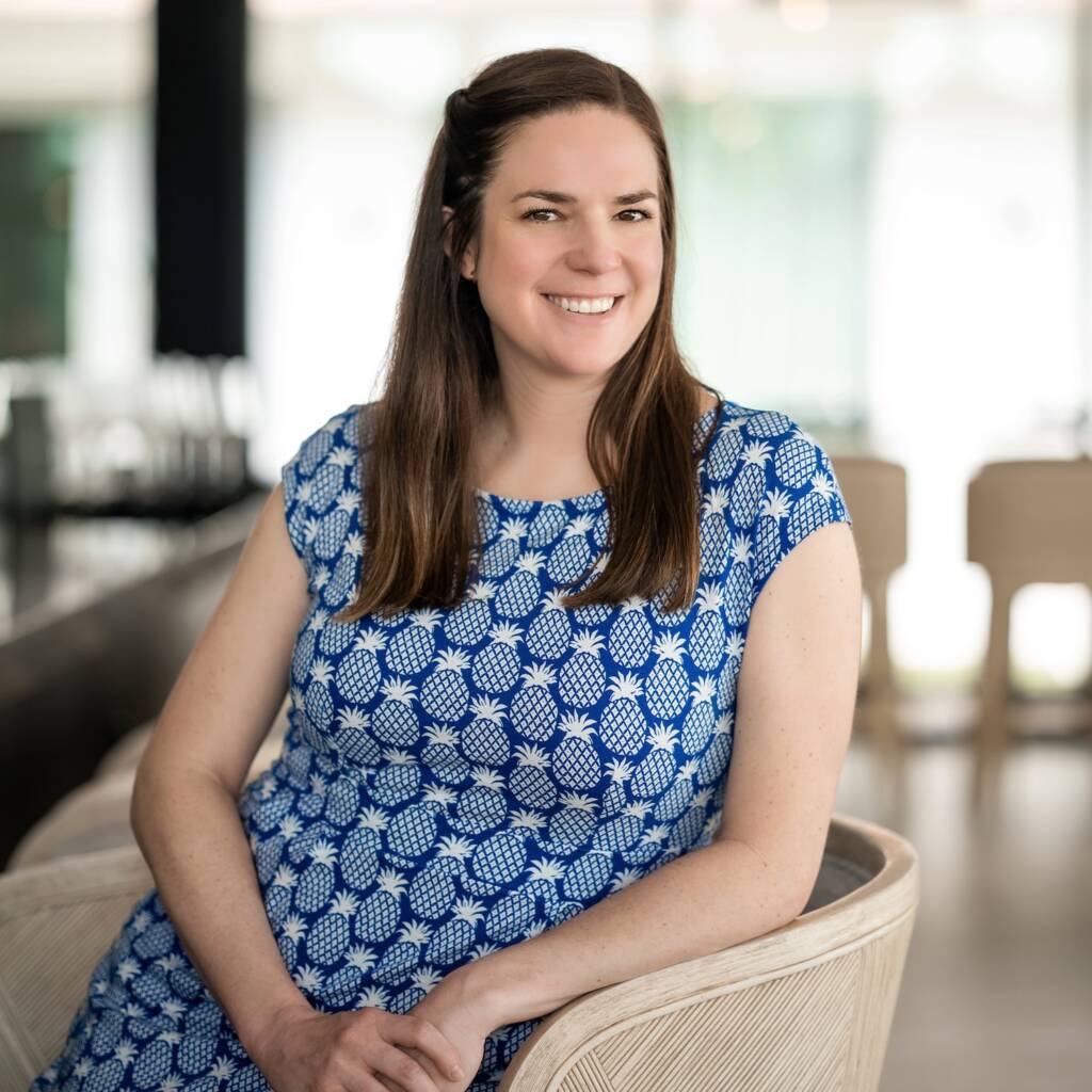 Melissa Bandel sits in a chair wearing a blue dress
